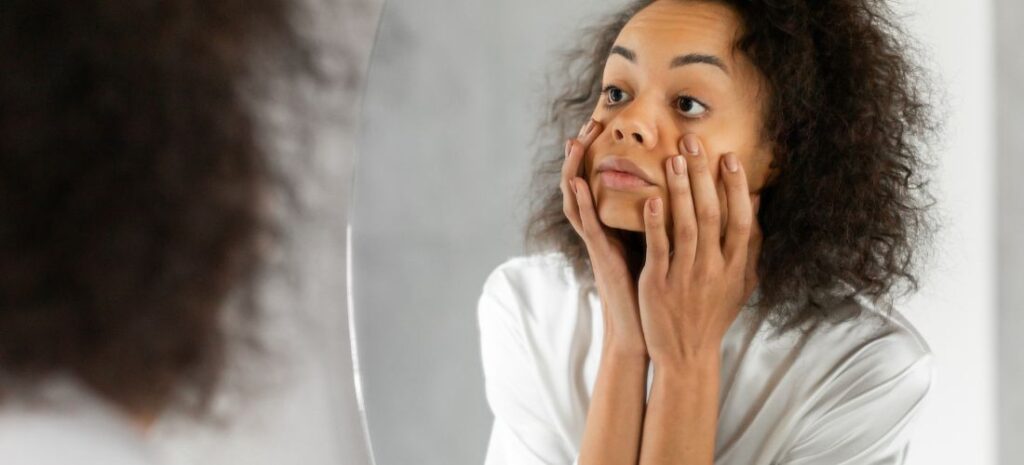 Woman examining her face in mirror, touching under eyes, dark circles, teeth whitening